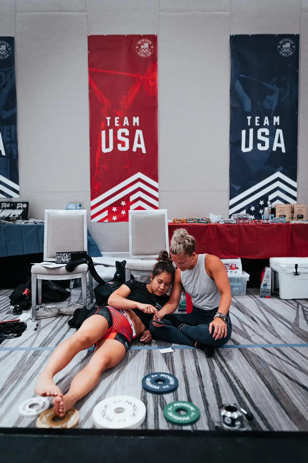 Morghan and another US Teammate relax on the floor looking at a phone together
