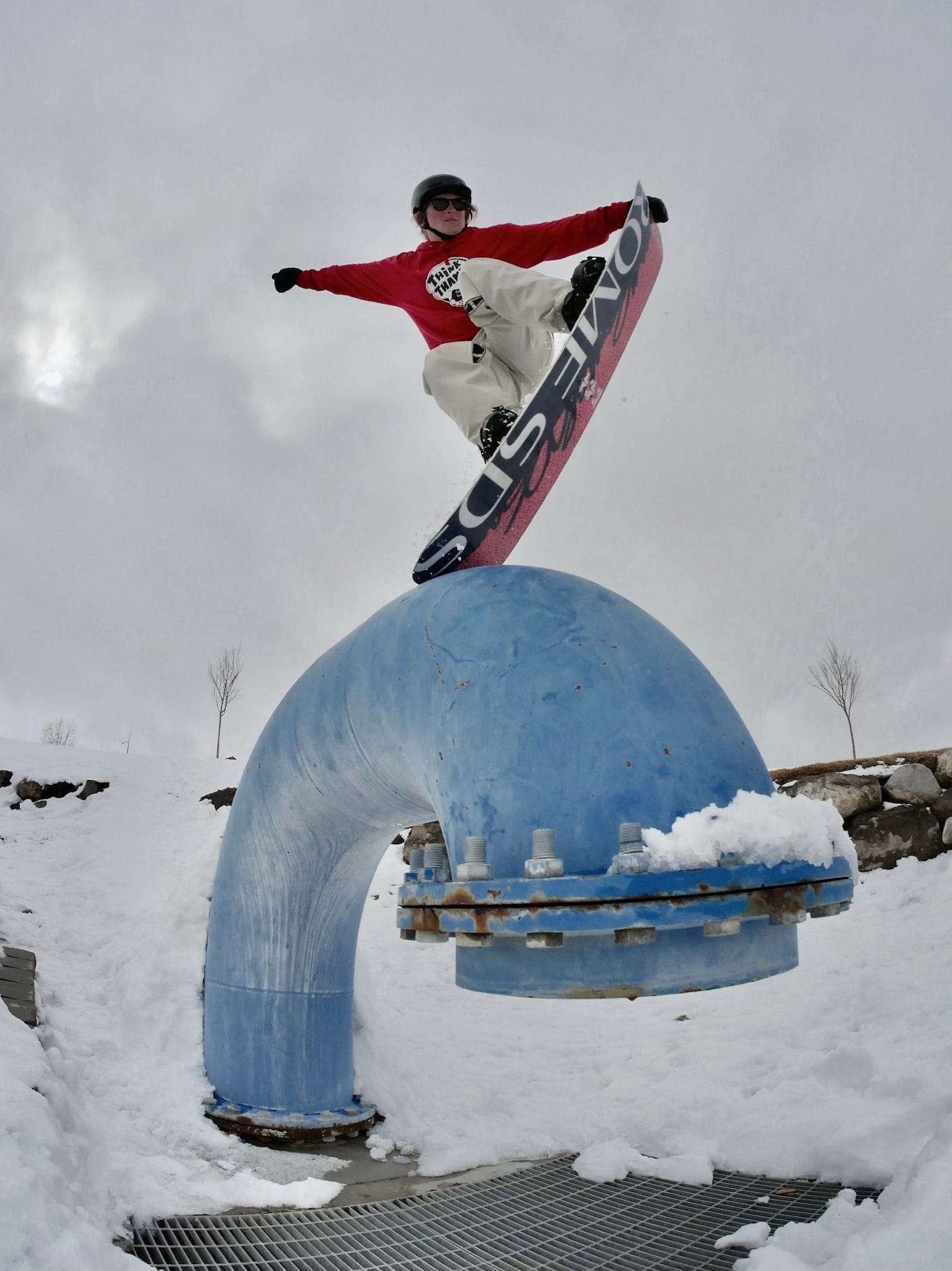 Madison does a snowboard trick over a large blue pipe