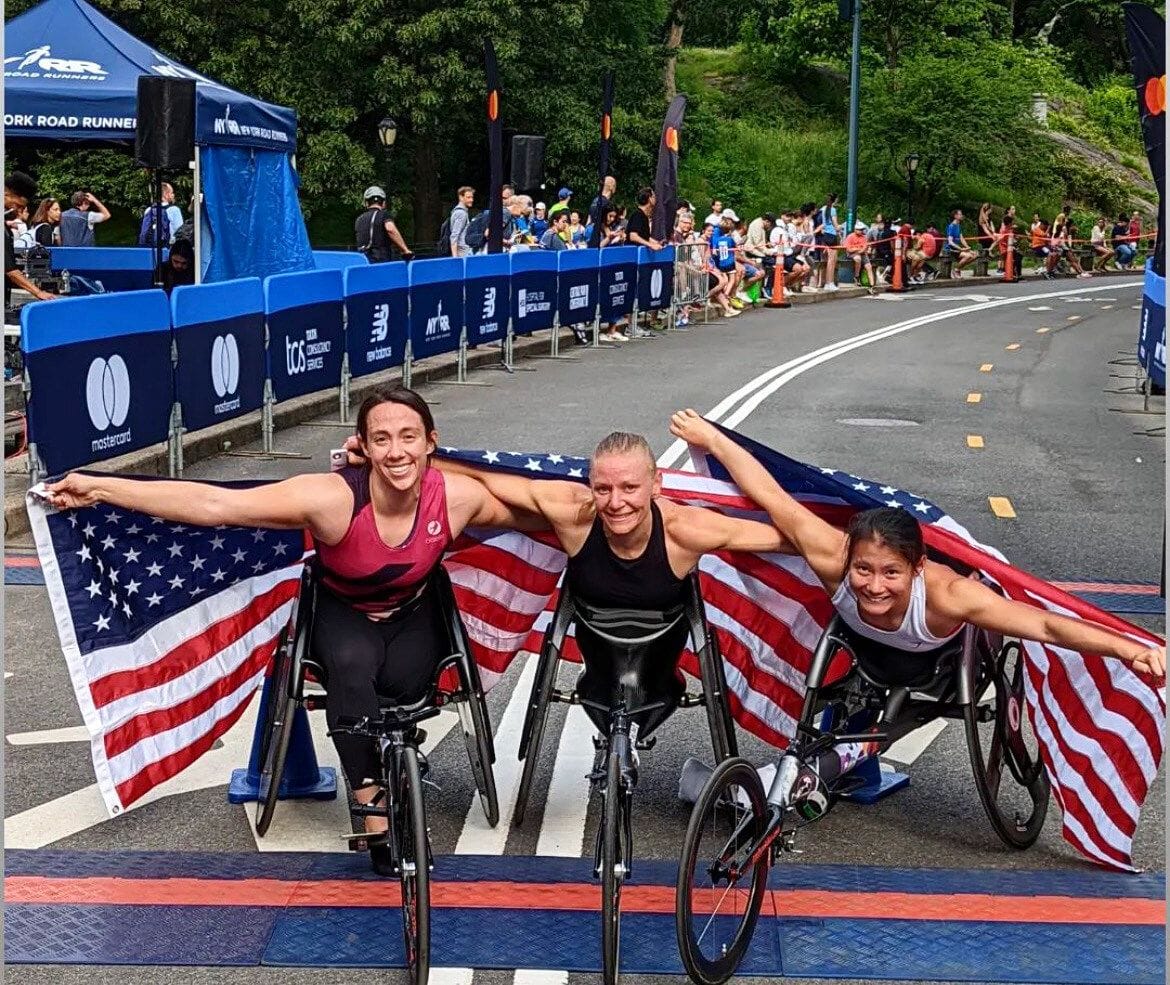 Hannah and 2 Paralympic US Teammates in racing wheelchairs holding US flags